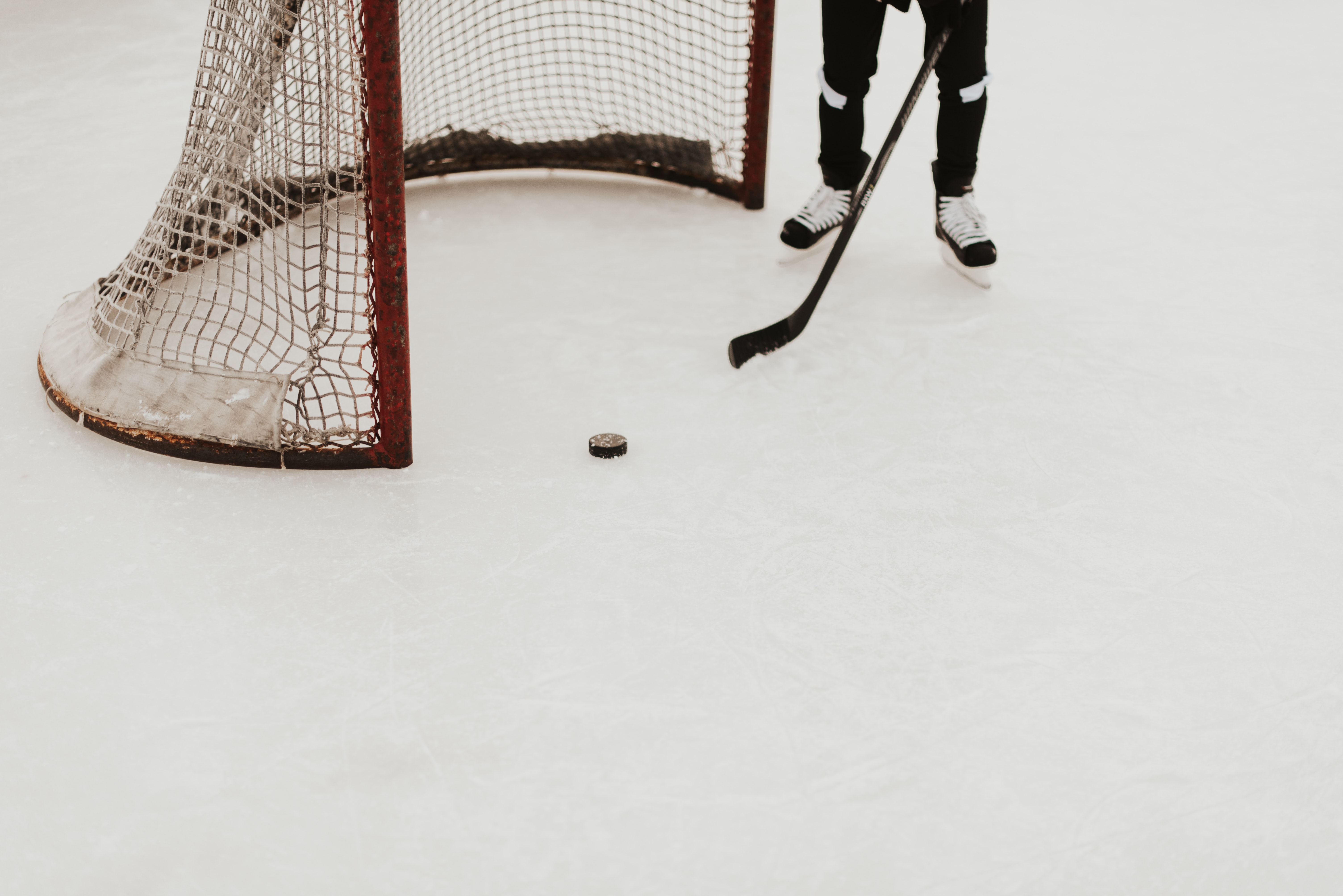 Detaljbild av hockeymål och spelare med klubba och puck på is.