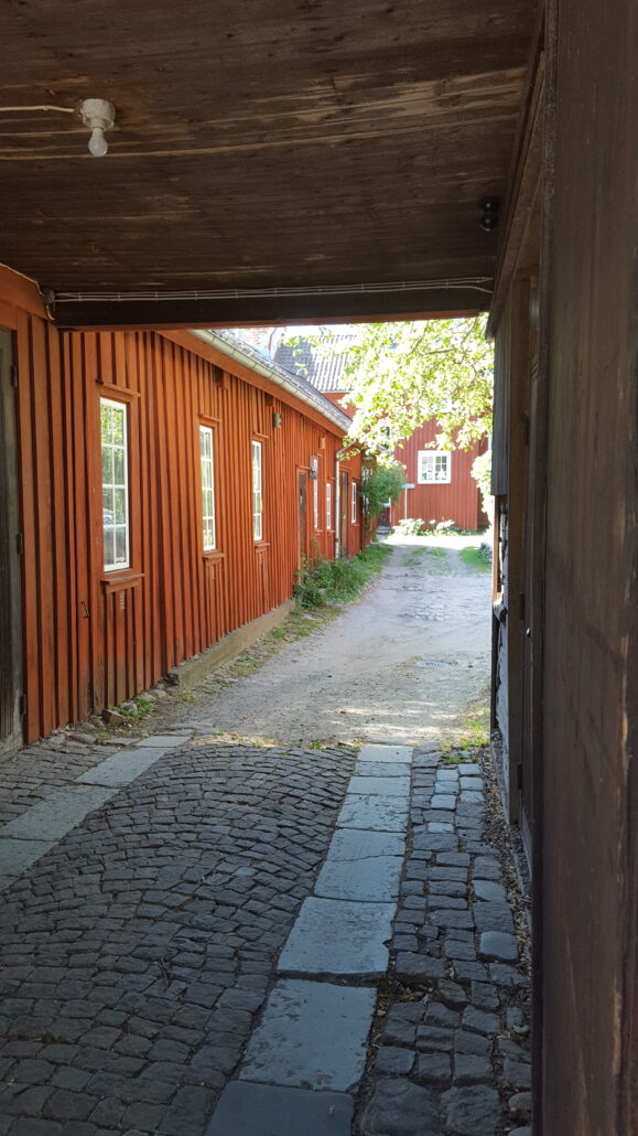 Gård längs Norra Ringgatan med röda trähus och grönskande träd.