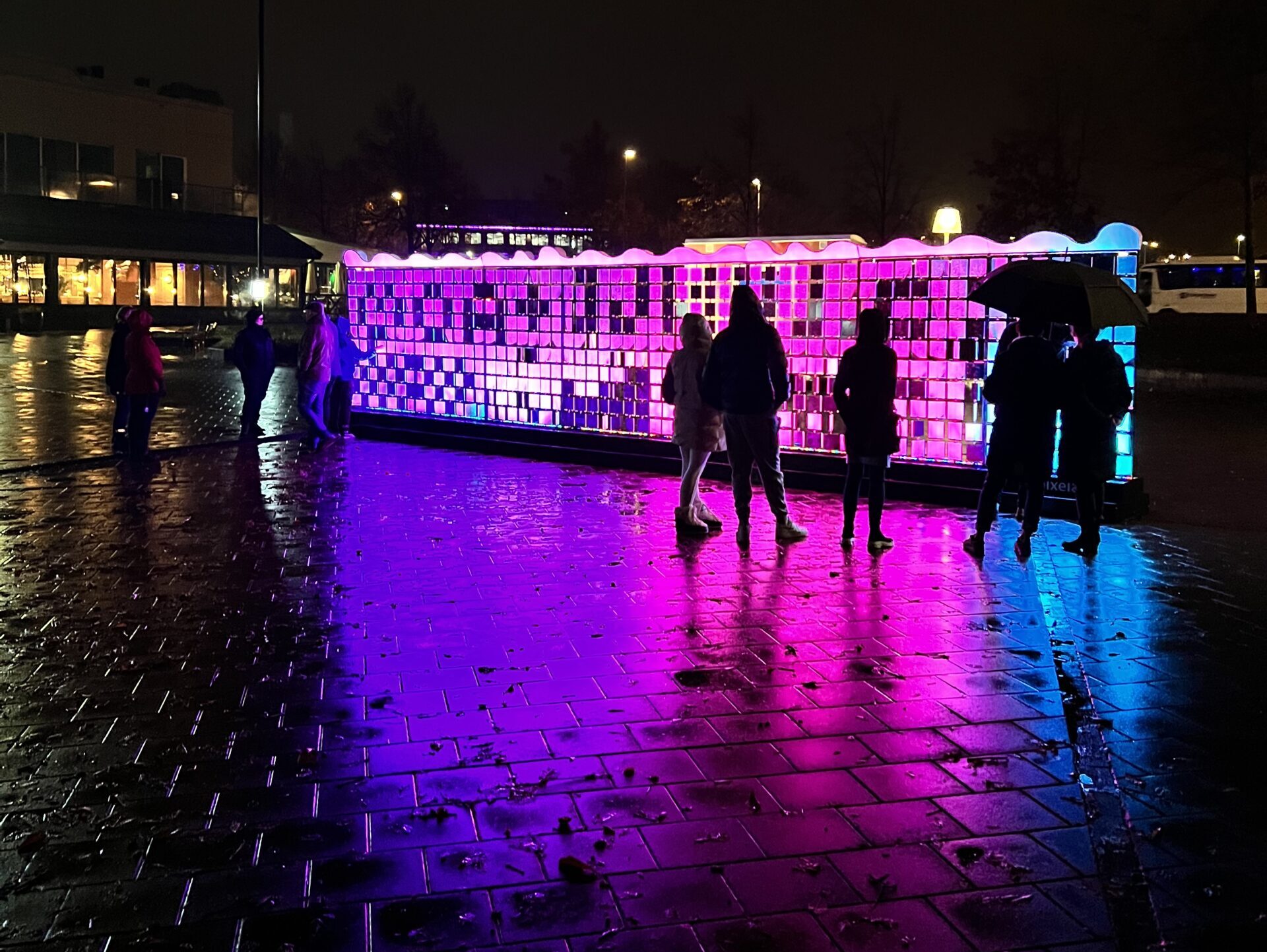 Lights in Alingsås 2022 i Åmanska parken framför Estrad Arena och Grand Hotel Alingsås en regnig kväll. Människor står framför ljuskonst med paraplyer.