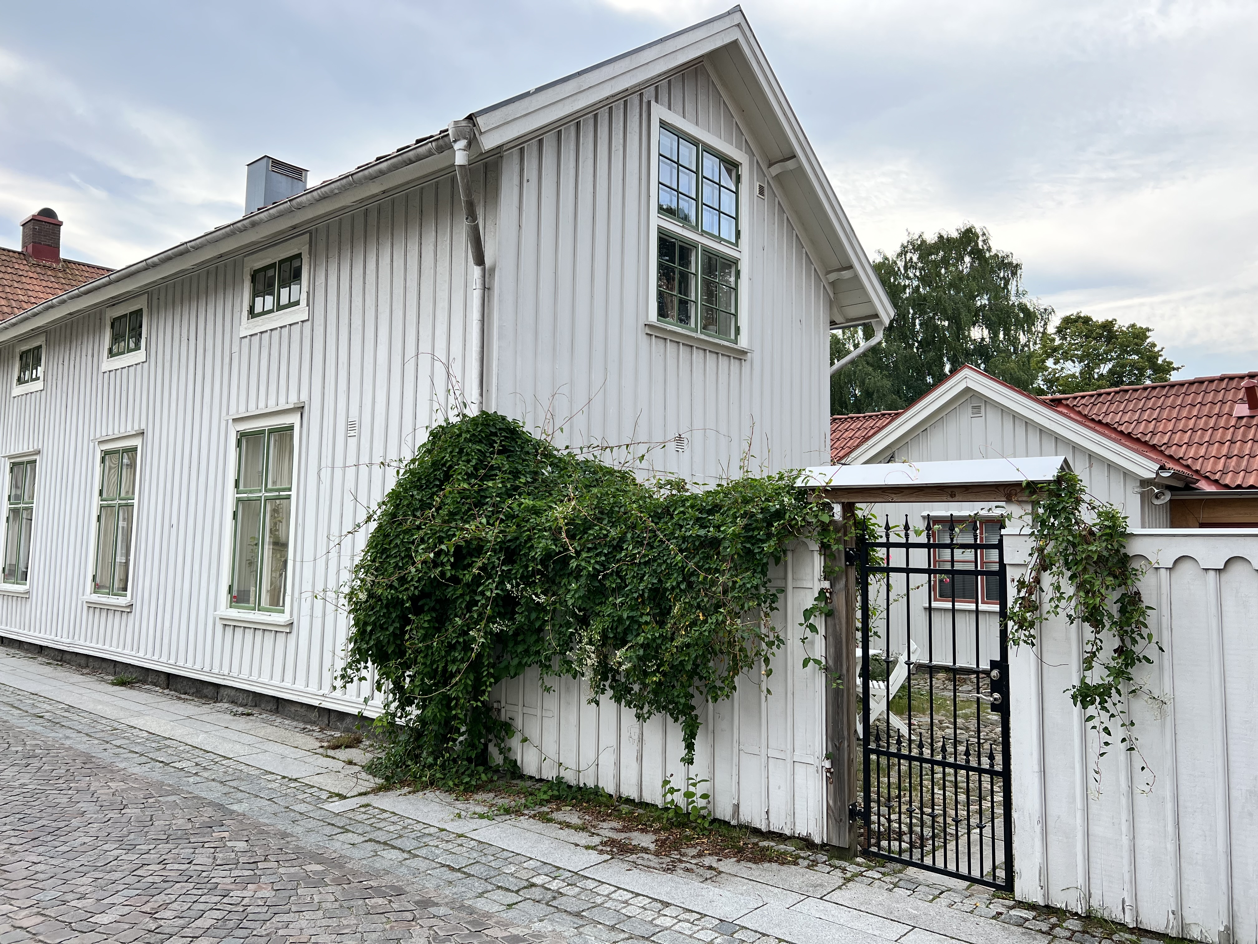 Gårdsentré på Färgaregatan i Alingsås stadskärna. Ljusgrå trähus och kullerstensgata.