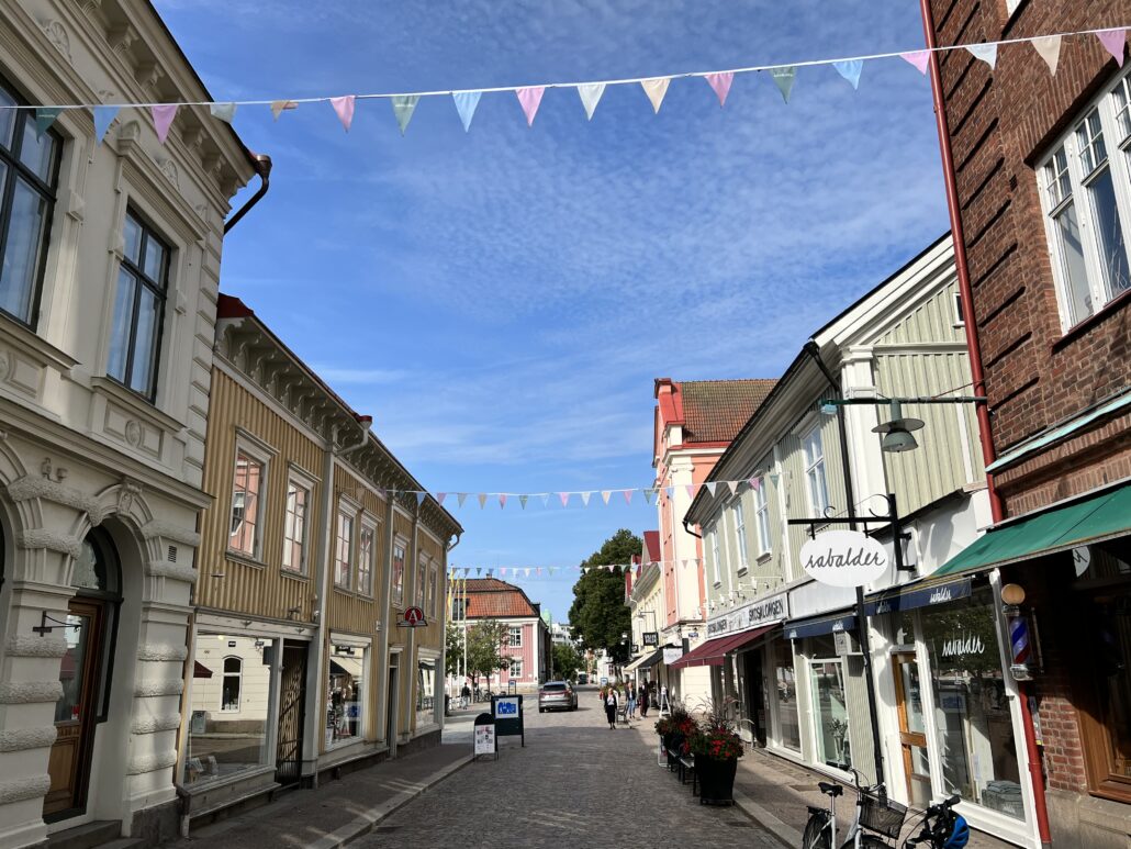 Sommar på Kungsgatan i Alingsås med blå himmel och färgglada vimplar hängandes över gatan.